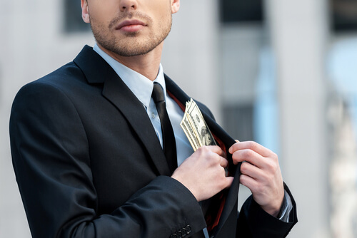 man putting a stack of cash in his suit pocket. potentially being charged for embezzlement